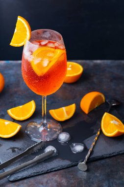 Aperol sprey kokteyli ve bar aksesuarları. İtalyan aperol sprey kokteyli ve koyu arkaplanda dilimlenmiş portakal. Yaz kokteyli aperol spreyini tahtaya serptim.