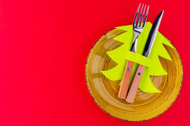 Noel çatal bıçak takımı. Kırmızı arka planda sarı tabak, çatal bıçak takımı ve kağıt Noel ağacı ile Noel masası. Üst görünüm