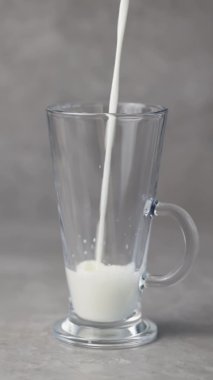 Süt gri arka plandaki bir bardağa dökülür. Süt ürünü konsepti. Dikey video