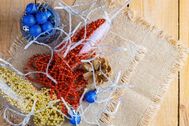 Noel boncuklu iki şampanya bardağı. Noel baloları ve çuval bezinin üzerindeki süslemeler. Ahşap arka planda çam kozalakları ve çok renkli boncuklar. Üst görünüm