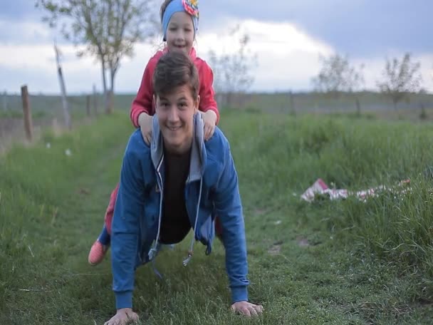 Ein junger Mann macht Liegestütze mit einem Mädchen auf dem Rücken — Stockvideo