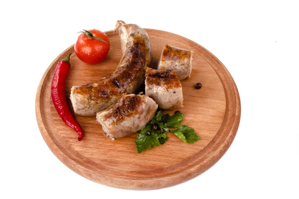 Gebratene Schweinswürste auf einem Holzteller mit Kirschtomaten und Paprika — Stockfoto