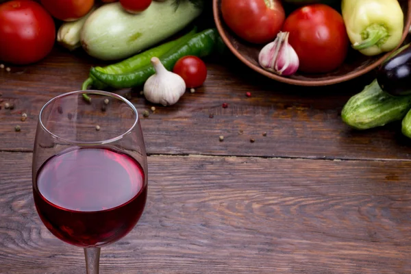Glas rött vin på en bakgrund av grönsaker — Stockfoto