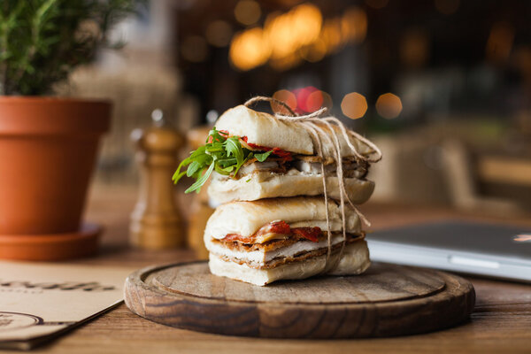 большой аппетитный сэндвич с рукколой и мясом на деревянной тарелке в ресторане
