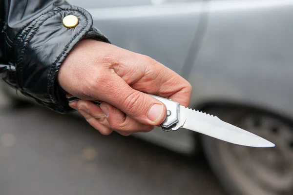 Folding knife in the hand of the criminal close-up. a man in a black jacket