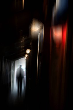 Yağmurlu bir gecede karanlık bir sokakta ceketli bir adamın silueti. Şiddet suçu ve zulüm teması. Bulanık etkisi