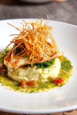 Buğulanmış balık, patates püresi, domates püresi ve beyaz tabakta sos.