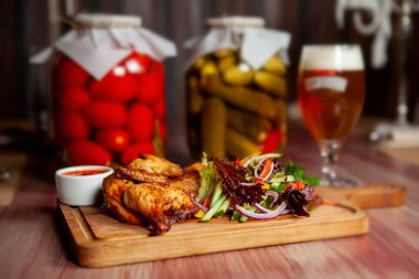 Kızarmış sulu tavuk, sebzeli ve otlu ve bardaki masada koyu renkli bir bardak light bira.