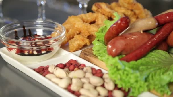 The food on the dish. Beer snacks on a wooden platter. Fried sausages, pistachios, sauce, green leaf lettuce. Squid rings in batter. Restaurant. Pub. Bar. — Stock Video