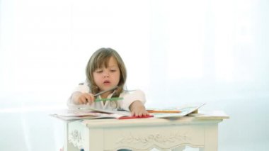 Küçük çocuklar kalemlerle oynar. Erkek ve kız pencerenin yanında resim çiziyorlar. Parlak giysiler giyen çocuklar masadaki kitaplarda resim çizdiler..