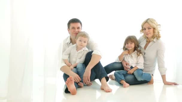 Feliz familia papá mamá niña y niño sentado en el suelo. Acurrucarse juntos. Padre con hijo, madre con hija, sonriendo, mirándose. Cortinas de luz y la ventana. Mucha luz. . — Vídeos de Stock