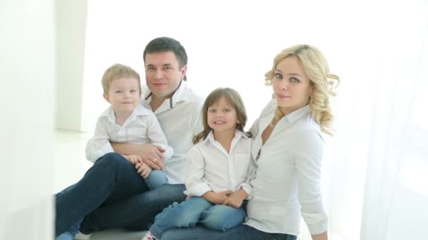 Feliz familia papá mamá niña y niño sentado en el suelo. Acurrucarse juntos. Padre con hijo, madre con hija, sonriendo, mirándose. Cortinas de luz y la ventana. Mucha luz. . — Vídeos de Stock