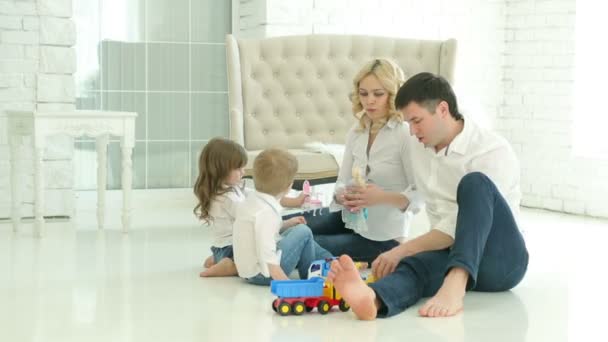 Aile birlikte oynar. Baba anne, oğul ve kızı birlikte oynuyorlar. Mutlu Avrupalı bir aile. Beyaz zemin ve kanepe, bir pencere ve beyaz tuğla duvarlar arka planda — Stok video