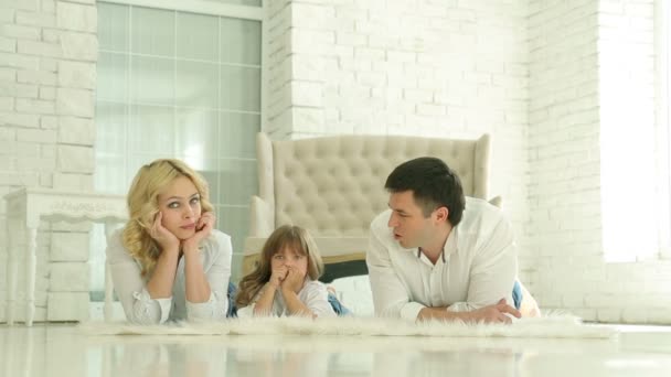 Papá, mamá y su hija yacen en el suelo. Feliz familia europea. En el fondo del suelo blanco y el sofá, una ventana y paredes de ladrillo blanco . — Vídeos de Stock