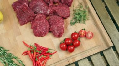 Ahşap tahta üzerinde biftek için taze et. Mermer et, sığır eti. Domates, biberiye, kekik, limon, kırmızı biber, kızılcık. Aşçı kızılcık tahtada dökülen, biberiye ete ekler.