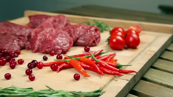 Frischfleisch für Steak auf Holzbrett. Marmoriertes Fleisch, Rind. in der Nähe von Tomaten, Rosmarin, Thymian, Zitrone, Paprika, Preiselbeere. der Koch gießt die Preiselbeere auf das Brett, fügt dem Fleisch Rosmarin hinzu. — Stockvideo