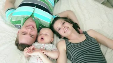 Mutlu bir aile. Anne baba ve altı aylık bebek. Yatakta yatan ve kameraya, seyir aile gülümseyen.