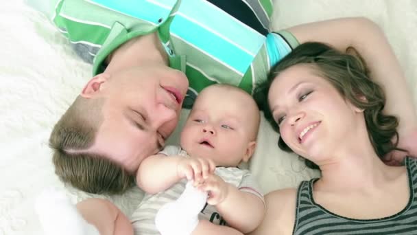 Glückliche Familie. Mama Papa und sechs Monate altes Baby. Familie liegt im Bett und blickt lächelnd in die Kamera. — Stockvideo