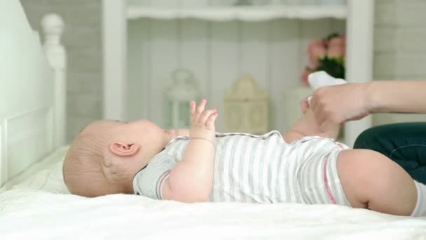 A mãe veste a criança. Uma jovem mãe e um filho de seis meses. Mãe usa fraldas, jeans e uma camisa, meias . — Vídeo de Stock