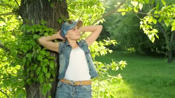 Menina bonita em jeans roupas posando ao pôr do sol na árvore na floresta . — Vídeo de Stock