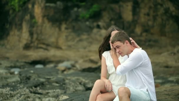 Paret sitter på klipporna vid en strand. — Stockvideo