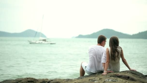 Pareja sentada en las rocas en una playa . — Vídeo de stock