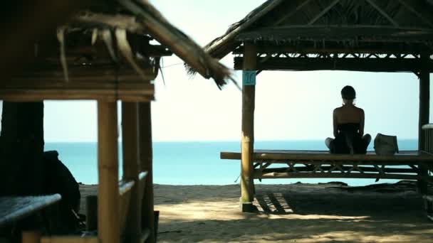 Silhouette young woman practicing yoga in pavilion in front of the beach. — Stock Video