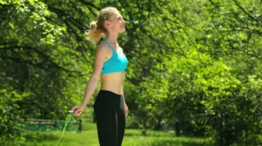 Kız bir egzersiz açık havada yapıyor. Kız bir gülümseme ile ip atlama üzerinde atlama. Genç kadın parkta egzersizleri yapıyor. İnce gövde ile şirin kız.