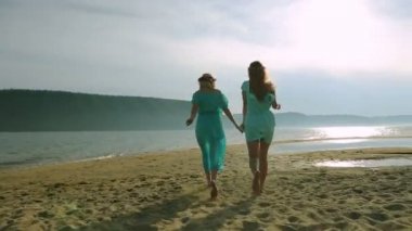 Etrafta dolanan ve kumsalda gün batımında atlama iki genç kadın silüeti. Dostluk, yaz tatili, tatil, parti ve insanlar kavramı - grup gülümseyen genç kızlar sahilde atlama.