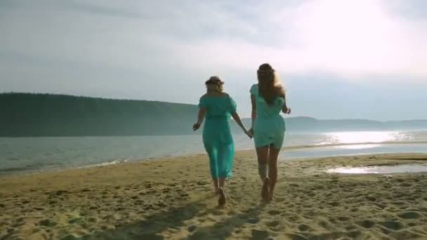 两个年轻女人跑来跑去，跳上沙滩日落时的剪影。友谊、 暑假、 假期、 党和人民的概念 — — 微笑的少女跳上海滩组. — 图库视频影像
