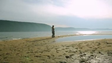 Etrafta dolanan ve kumsalda gün batımında atlama genç kadın silüeti.