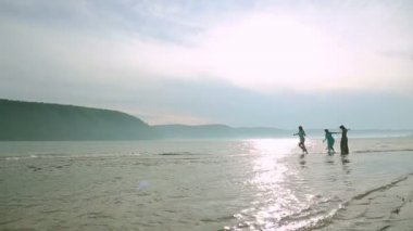 Parti ve insanlar kavramı - genç kızlar sahilde atlama gülümseyen bir grup. Etrafta dolanan ve kumsalda gün batımında atlama üç genç kadın silüeti.