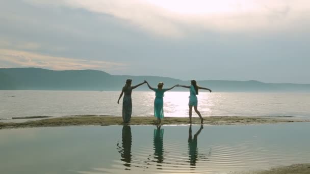 Concepto de fiesta y gente - grupo de adolescentes sonrientes saltando a la playa. Silueta de tres mujeres jóvenes corriendo y saltando en la playa de arena al atardecer . — Vídeo de stock