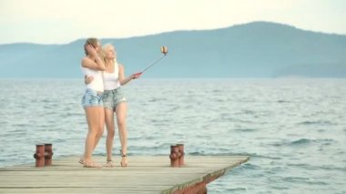 İki arkadaş kadın cep telefonu ile selfie nehir kenarında alarak. Nehir kenarında zevk ve selfie kullanarak alarak iki genç kız akıllı telefon.