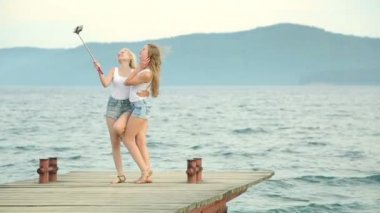 İki arkadaş kadın cep telefonu ile selfie nehir kenarında alarak. Nehir kenarında zevk ve selfie kullanarak alarak iki genç kız akıllı telefon.