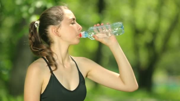 Mujer joven y delgada bebiendo agua después del entrenamiento. La atleta se toma un descanso, bebe agua, corre en un día caluroso . — Vídeos de Stock