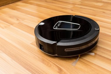 Robotic vacuum cleaner on wood parquet floor.
