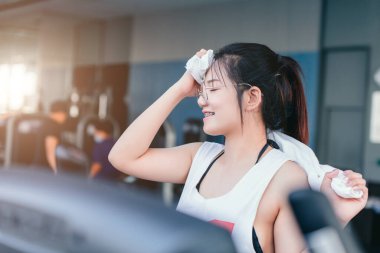 Asian braces girl using towel wiped her sweat after exercise in sport club every morning, she feel happy and smile after workout.