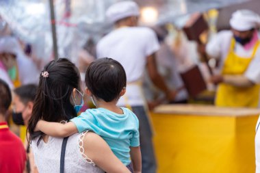 Thai mother bring their children to travel watching the cooking intently in Vegetarian Festival on Yaowarat Road. 18 October 2020, Bangkok,THAILAND.