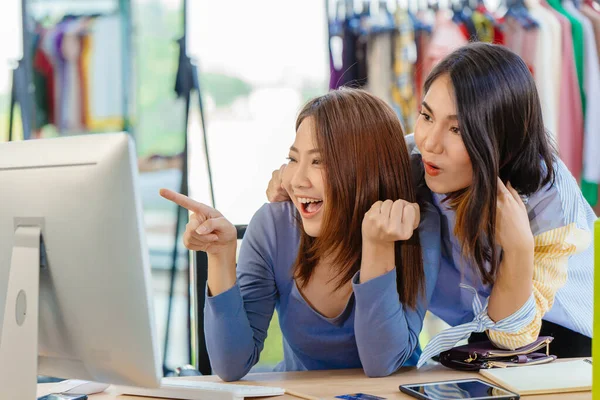 Asian woman with friend exciting hand pointing at computer screen for happy young SME business owner concept.
