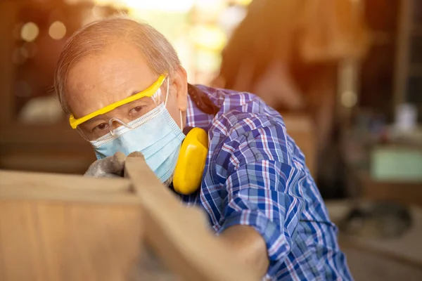 優れた退職のための高齢労働者木工引退趣味 フェイスマスク保護と木製家具を作るのアジアの男性成熟したプロのマスター — ストック写真