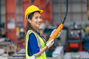 Portre, genç Asyalı kadın mühendis mutlu gülümseyen profesyonel vinç operatörü ağır sanayi fabrikasında güvenlik başlığı takmış.
