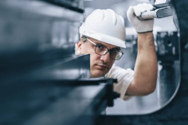 Üst düzey mühendis kalite kontrol ürünlerine bakar, metal levha fabrikasında profesyonel işler, metal parçalarında seçici odak