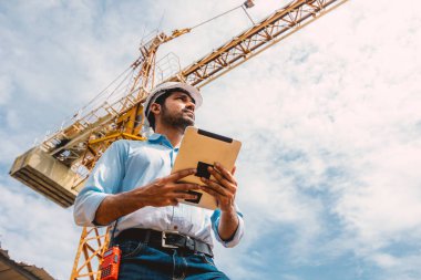 Hintli inşaat mühendisi inşaat alanı kontrol operasyonu. Foreman, vinçle tableti tutuyor..