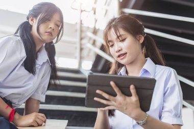 Üniformalı akıllı öğrenci kadınlar modern okul kampüsündeki tabletlerle ev ödevlerini tartışıyor. Taylandlı liseli kız öğrenci.