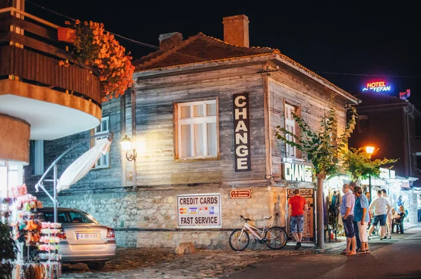 La gente cammina per il centro storico di notte. Cambio valuta in una tipica casa in legno nell'antica città di Nessebar . — Foto Stock