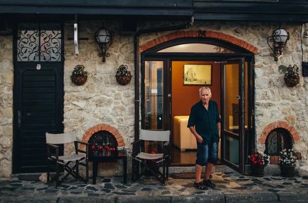 Viejo se para cerca del hotel en el casco antiguo de Nessebar y mira a los transeúntes . — Foto de Stock