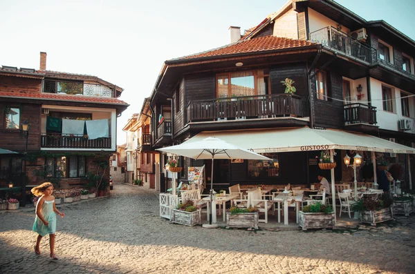 Flickan kör genom gatorna i gamla Nesebar café och butiker i solnedgången. — Stockfoto