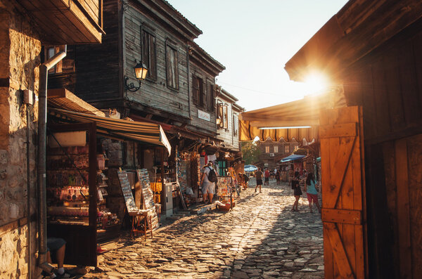 People walk through streets of ancient nesebar at sunset. 