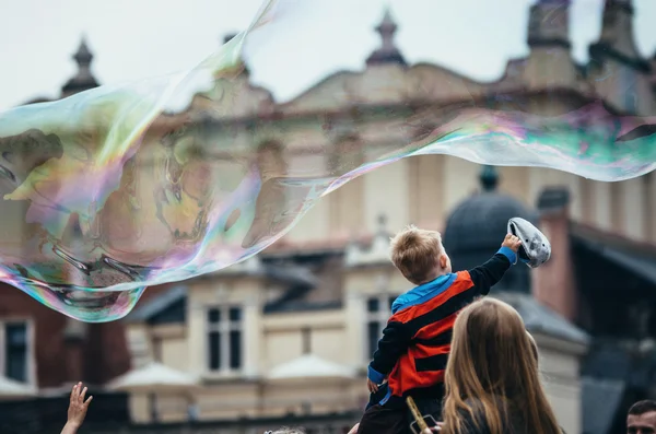 Мальчик сидел на папиных плечах и трогал гигантские пузыри — стоковое фото